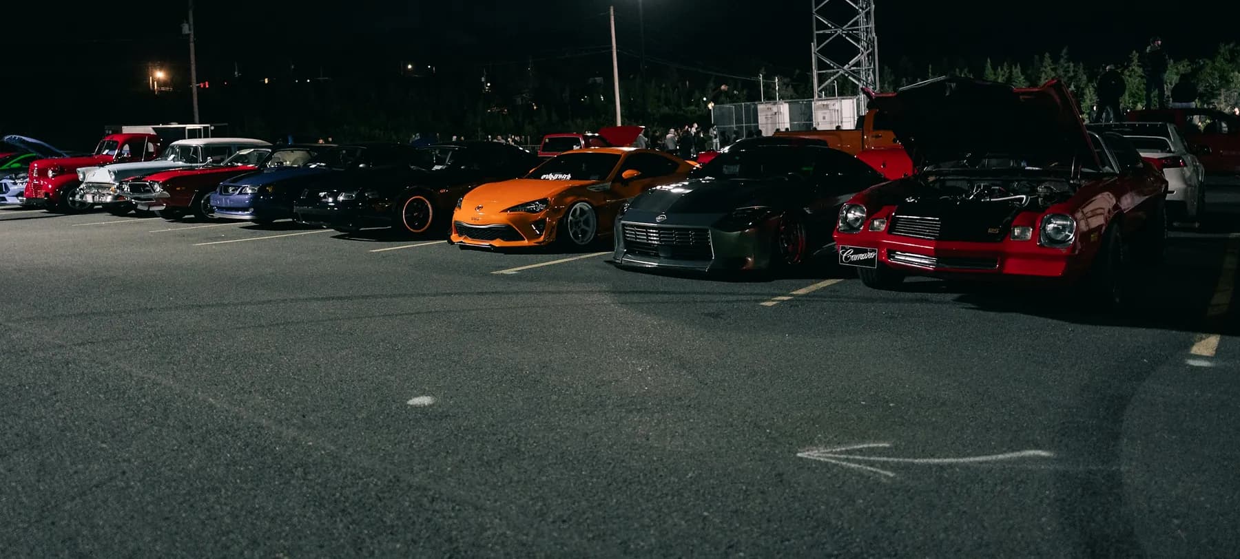 A night meet in a car park: a row of modified cars under floodlights