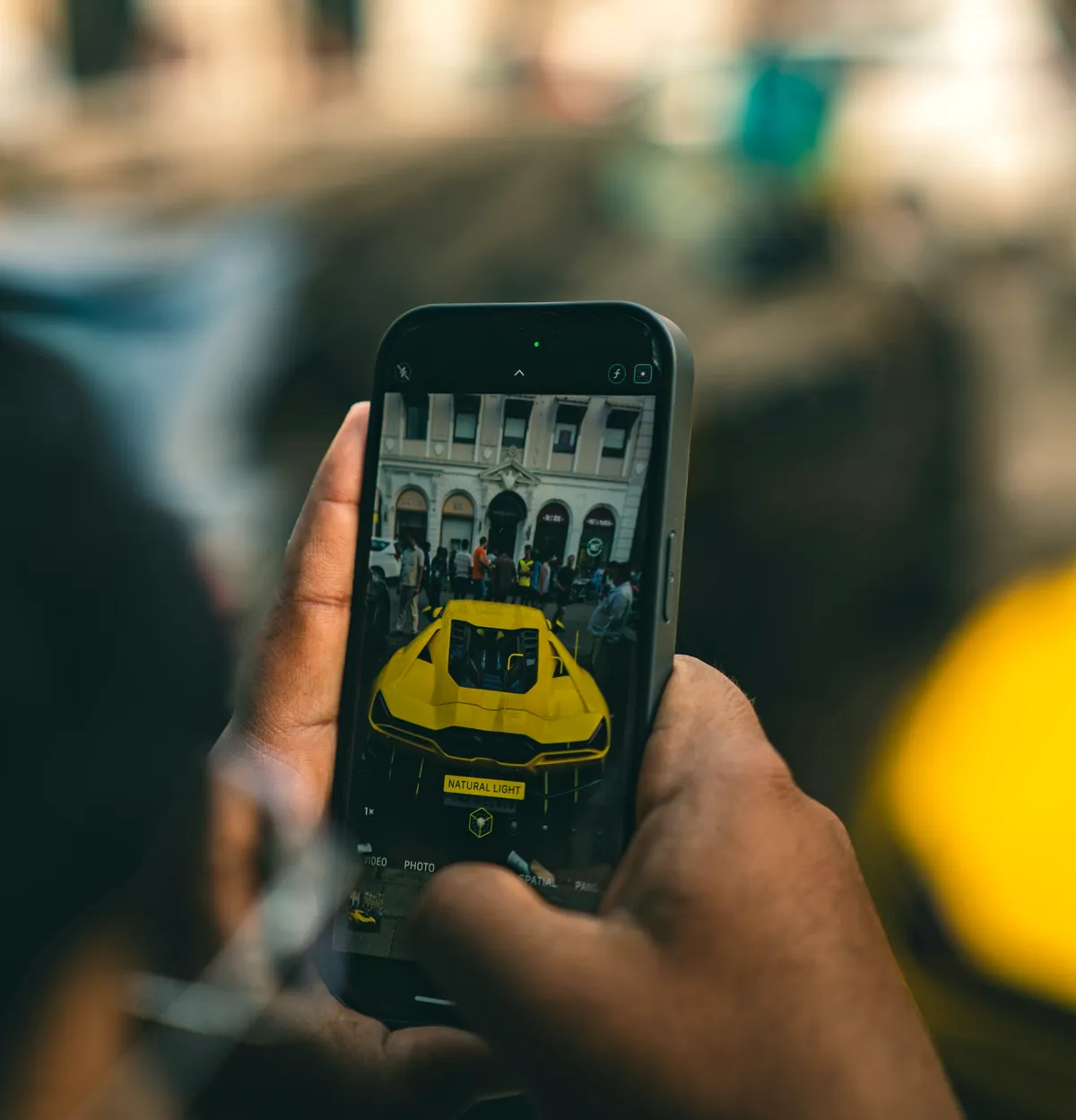A phone held up at a street meet, framing a yellow supercar on screen